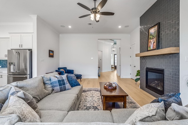 living room with light hardwood / wood-style floors, ceiling fan, ornamental molding, and a tiled fireplace