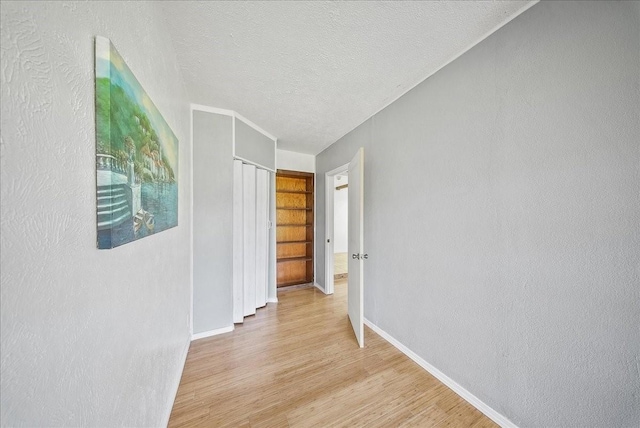 corridor with a textured ceiling and light hardwood / wood-style floors