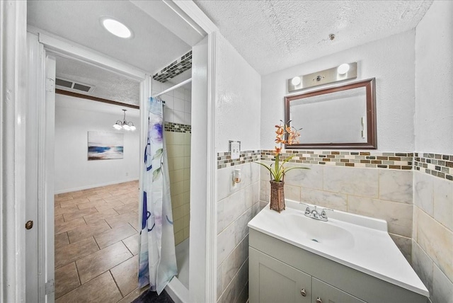 bathroom with walk in shower, vanity, a textured ceiling, tile walls, and a notable chandelier