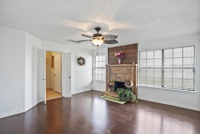 unfurnished living room featuring a textured ceiling, dark hardwood / wood-style flooring, a brick fireplace, and ceiling fan