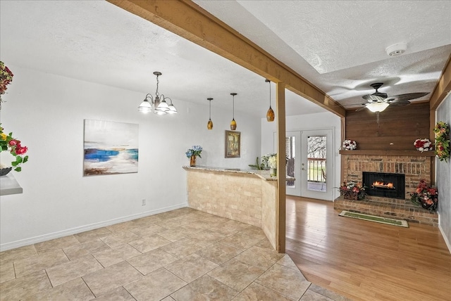 interior space featuring ceiling fan with notable chandelier, light wood-type flooring, a textured ceiling, and a brick fireplace