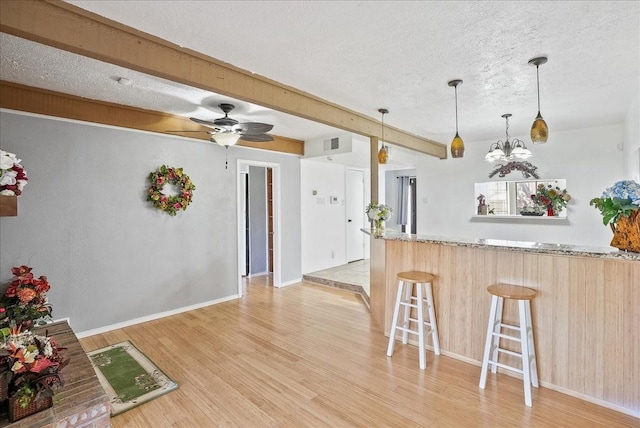 kitchen with light stone countertops, hanging light fixtures, beamed ceiling, light hardwood / wood-style floors, and a kitchen bar