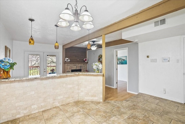 kitchen with ceiling fan with notable chandelier, hanging light fixtures, a brick fireplace, a textured ceiling, and french doors