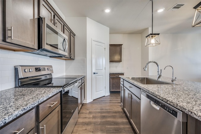 kitchen with light stone counters, sink, decorative light fixtures, and stainless steel appliances