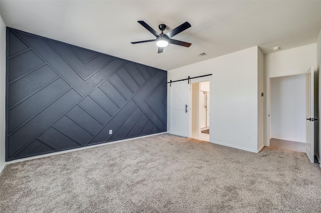 unfurnished bedroom with a barn door, light carpet, and ceiling fan