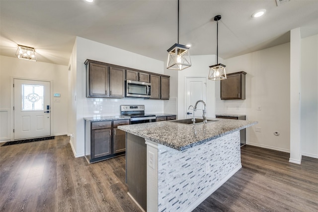 kitchen featuring sink, stone countertops, a center island with sink, appliances with stainless steel finishes, and pendant lighting