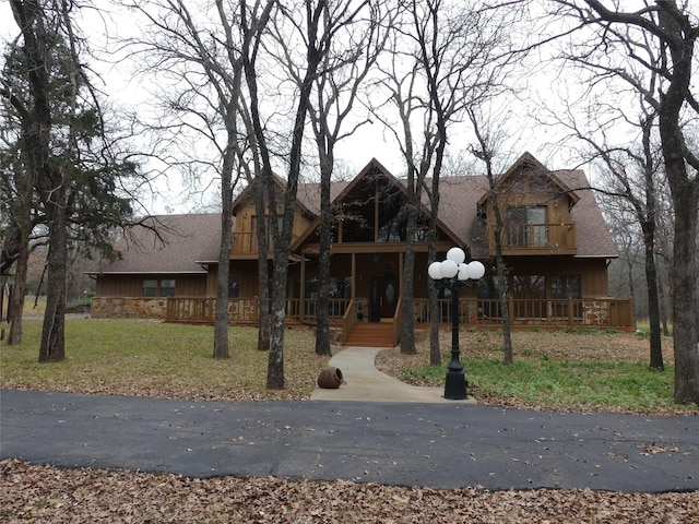 view of front facade with a shingled roof, a front yard, stone siding, and a balcony