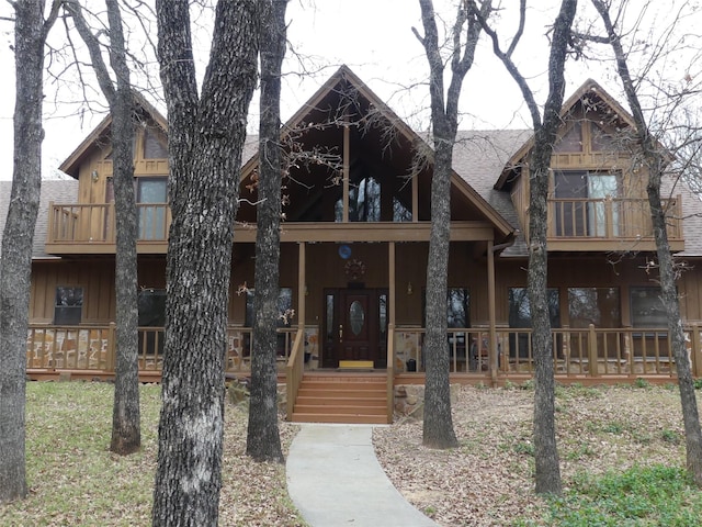 view of front facade with covered porch, roof with shingles, and a balcony