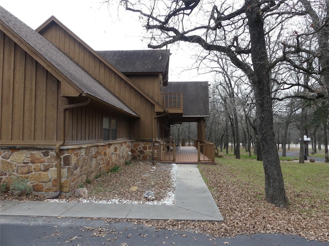 view of property exterior featuring a shingled roof, board and batten siding, a deck, a balcony, and stone siding