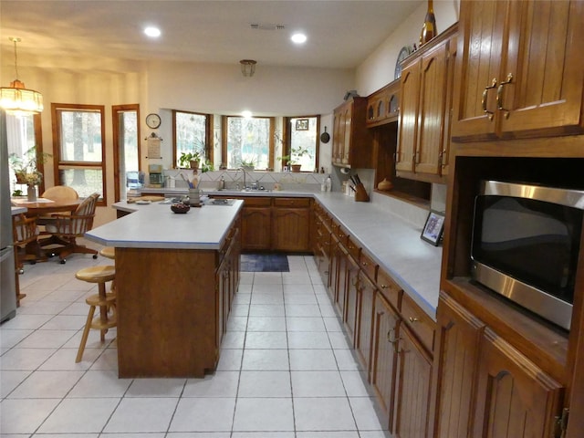 kitchen with visible vents, stainless steel microwave, backsplash, brown cabinetry, and a kitchen bar