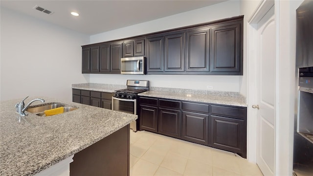 kitchen with sink, light stone counters, dark brown cabinets, light tile patterned floors, and appliances with stainless steel finishes