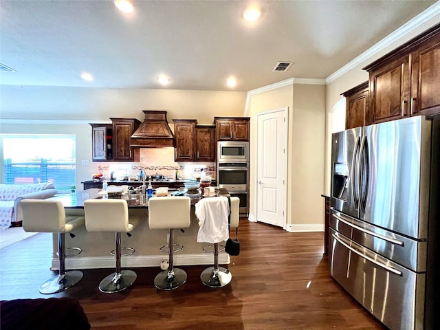 kitchen featuring a kitchen bar, appliances with stainless steel finishes, dark hardwood / wood-style flooring, custom range hood, and a kitchen island with sink