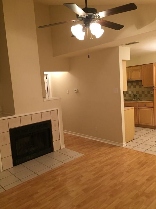 unfurnished living room with ceiling fan, light hardwood / wood-style floors, sink, and a tiled fireplace