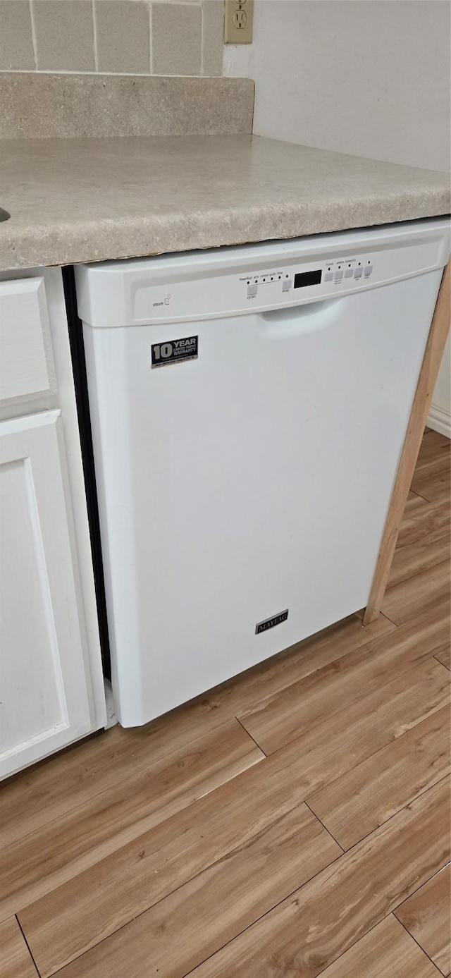 interior details with white cabinets, white dishwasher, and light hardwood / wood-style flooring