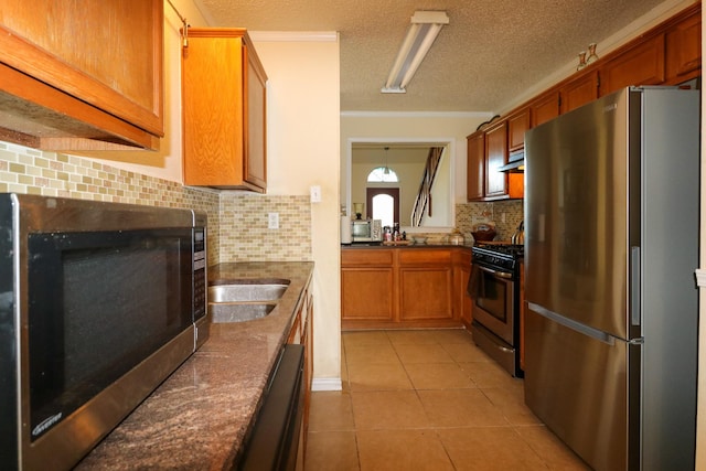 kitchen featuring appliances with stainless steel finishes, backsplash, a textured ceiling, crown molding, and light tile patterned floors