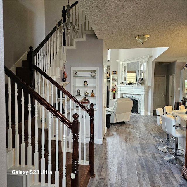 staircase featuring a fireplace, wood-type flooring, and a textured ceiling