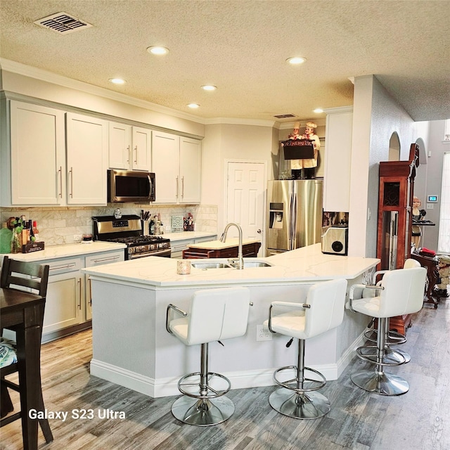 kitchen with a kitchen bar, a textured ceiling, stainless steel appliances, sink, and light hardwood / wood-style floors