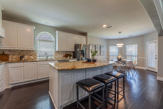 kitchen featuring stainless steel refrigerator with ice dispenser, white cabinetry, decorative light fixtures, and a center island