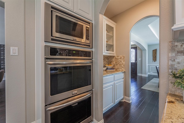 kitchen with tasteful backsplash, dark hardwood / wood-style flooring, stainless steel appliances, light stone countertops, and white cabinets