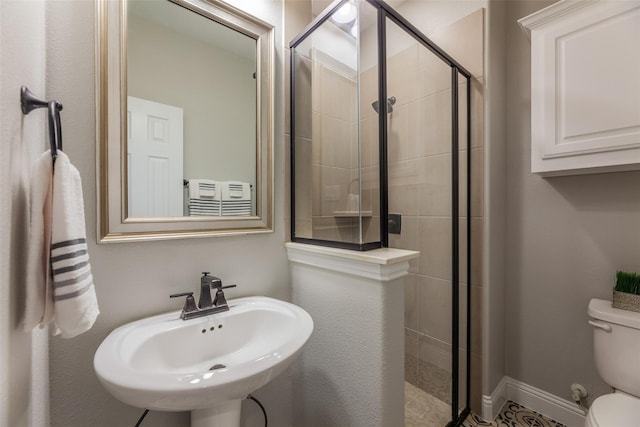 bathroom featuring a shower with shower door, sink, and toilet