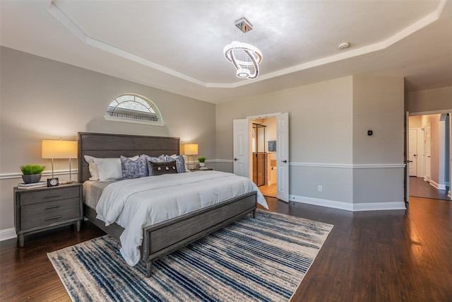 bedroom featuring dark hardwood / wood-style flooring, a notable chandelier, a tray ceiling, and ensuite bath