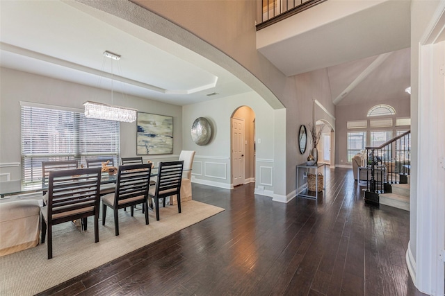 dining room featuring a tray ceiling, dark wood-type flooring, a chandelier, and a towering ceiling