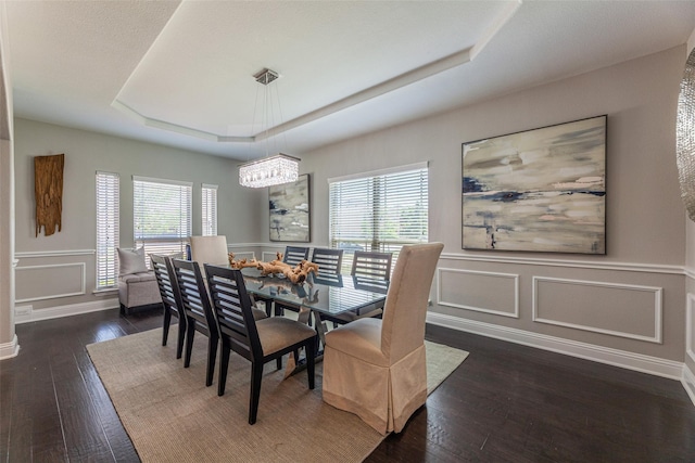 dining room featuring a healthy amount of sunlight, dark wood-type flooring, and a tray ceiling