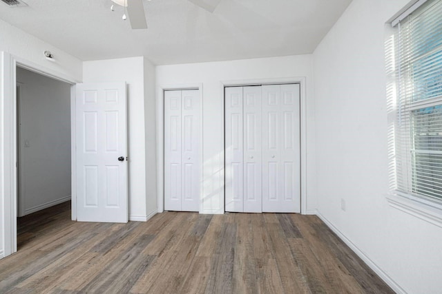 unfurnished bedroom featuring ceiling fan, dark hardwood / wood-style flooring, and multiple closets