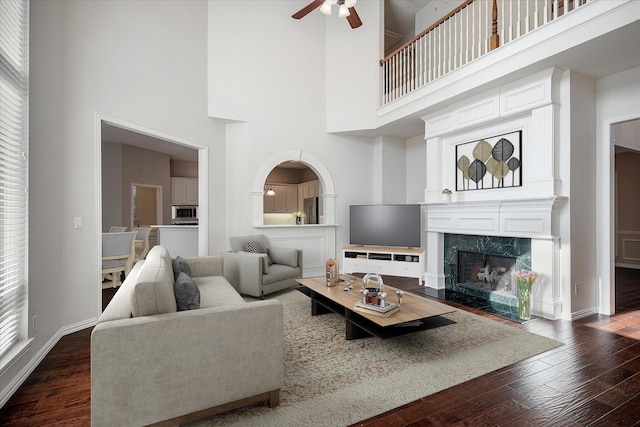 living room with ceiling fan, a towering ceiling, a premium fireplace, and dark wood-type flooring