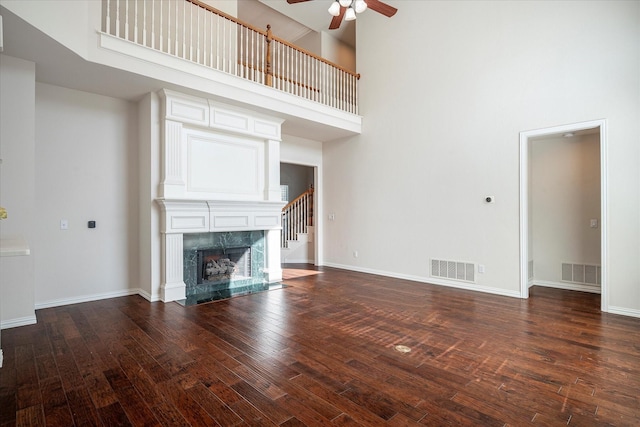 unfurnished living room featuring ceiling fan, dark wood-type flooring, a premium fireplace, and a towering ceiling