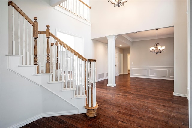 entryway with decorative columns, dark hardwood / wood-style floors, ornamental molding, and an inviting chandelier