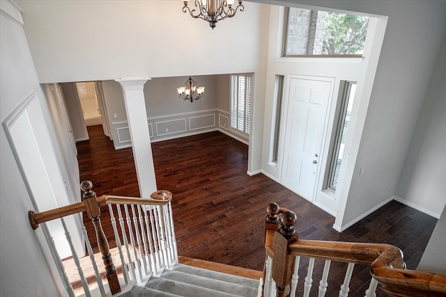 entrance foyer with ornate columns, a towering ceiling, dark hardwood / wood-style floors, and an inviting chandelier