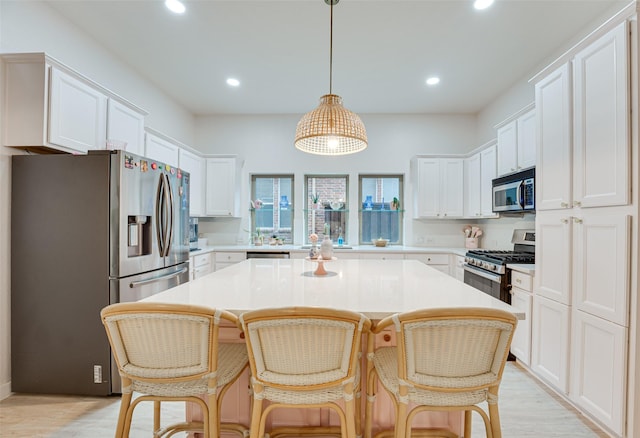 kitchen with a center island, decorative light fixtures, a kitchen bar, white cabinetry, and stainless steel appliances