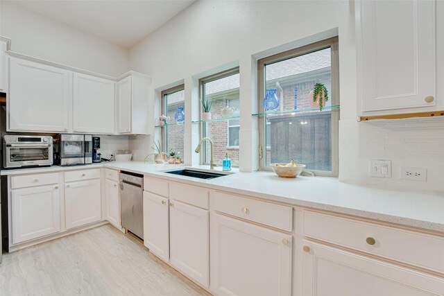 kitchen featuring white cabinetry, sink, stainless steel dishwasher, decorative backsplash, and light wood-type flooring