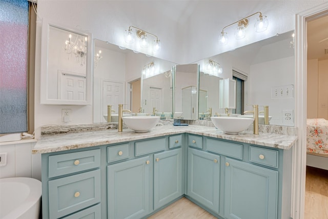 bathroom with a notable chandelier, vanity, a bathtub, and wood-type flooring