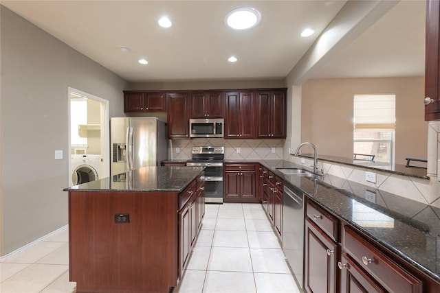 kitchen with washer / clothes dryer, sink, stainless steel appliances, and dark stone counters