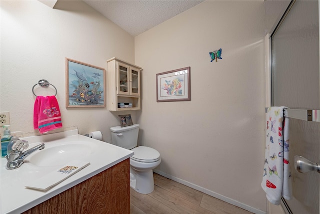 full bathroom with vanity, toilet, a shower with shower door, a textured ceiling, and wood finished floors