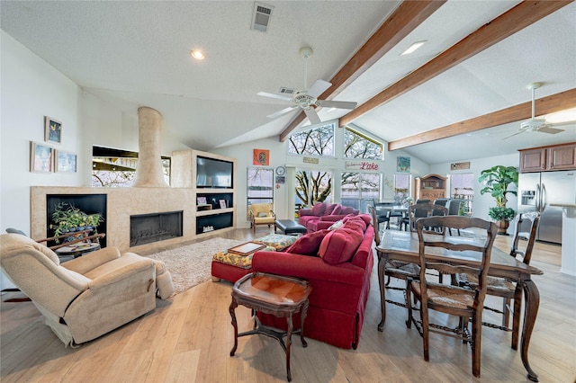 living room with ceiling fan, a fireplace, light hardwood / wood-style floors, a textured ceiling, and beamed ceiling