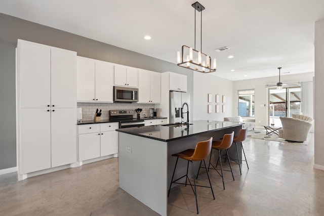 kitchen featuring white cabinetry, hanging light fixtures, an island with sink, and appliances with stainless steel finishes