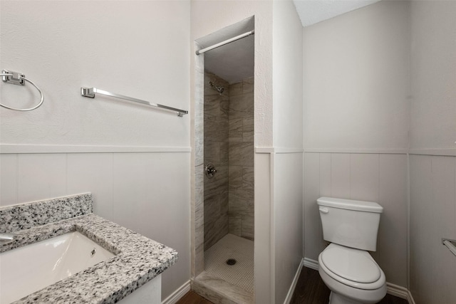 bathroom featuring a tile shower, vanity, and toilet