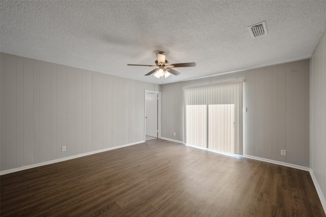 empty room featuring a textured ceiling, wooden walls, ceiling fan, and dark wood-type flooring