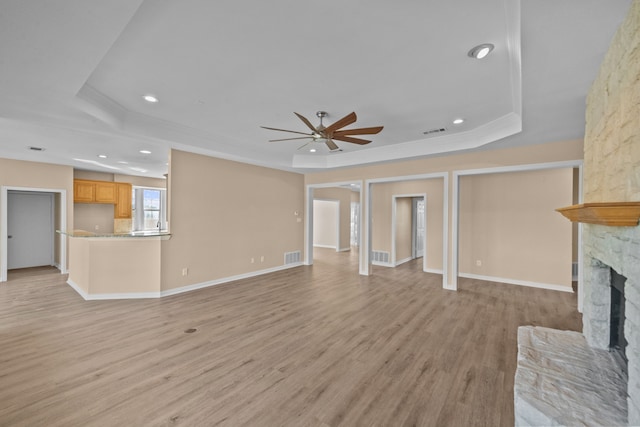 unfurnished living room featuring a raised ceiling, ceiling fan, a fireplace, and light hardwood / wood-style floors