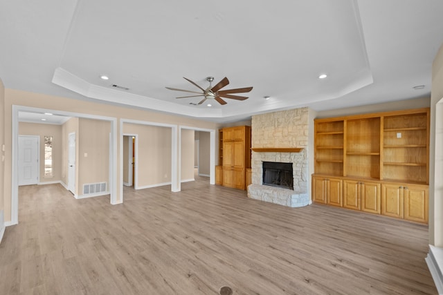 unfurnished living room featuring ceiling fan, light hardwood / wood-style flooring, a raised ceiling, and a stone fireplace