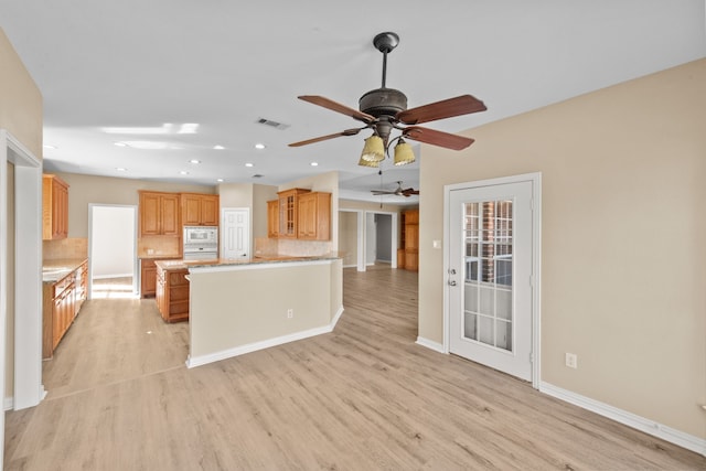 kitchen featuring kitchen peninsula, ceiling fan, tasteful backsplash, white appliances, and light wood-type flooring