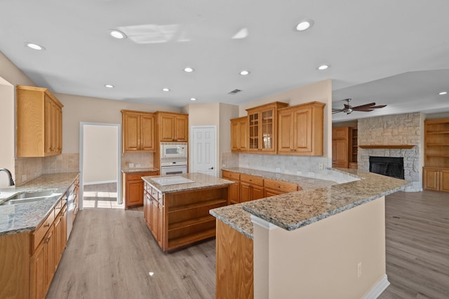 kitchen featuring a fireplace, a kitchen island, kitchen peninsula, sink, and white appliances