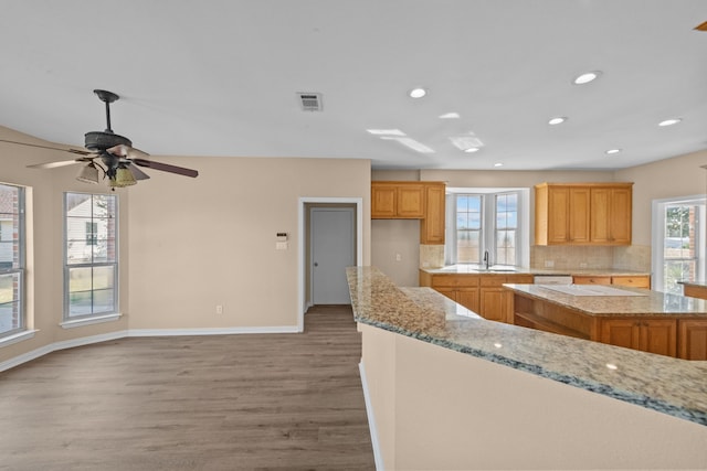 kitchen featuring a center island, tasteful backsplash, ceiling fan, light wood-type flooring, and light stone counters