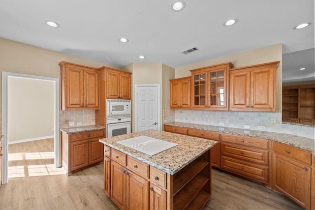 kitchen featuring backsplash, a center island, white appliances, light wood-type flooring, and light stone countertops