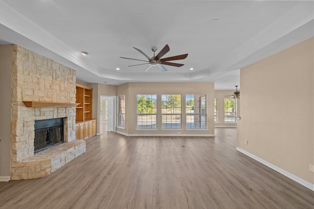 unfurnished living room featuring ceiling fan, a stone fireplace, a tray ceiling, and hardwood / wood-style floors