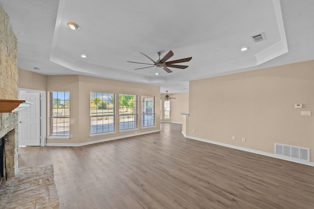 unfurnished living room with a raised ceiling, ceiling fan, a fireplace, and wood-type flooring