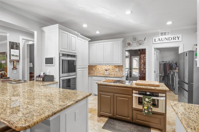 kitchen featuring washing machine and dryer, stainless steel appliances, white cabinetry, and a kitchen island